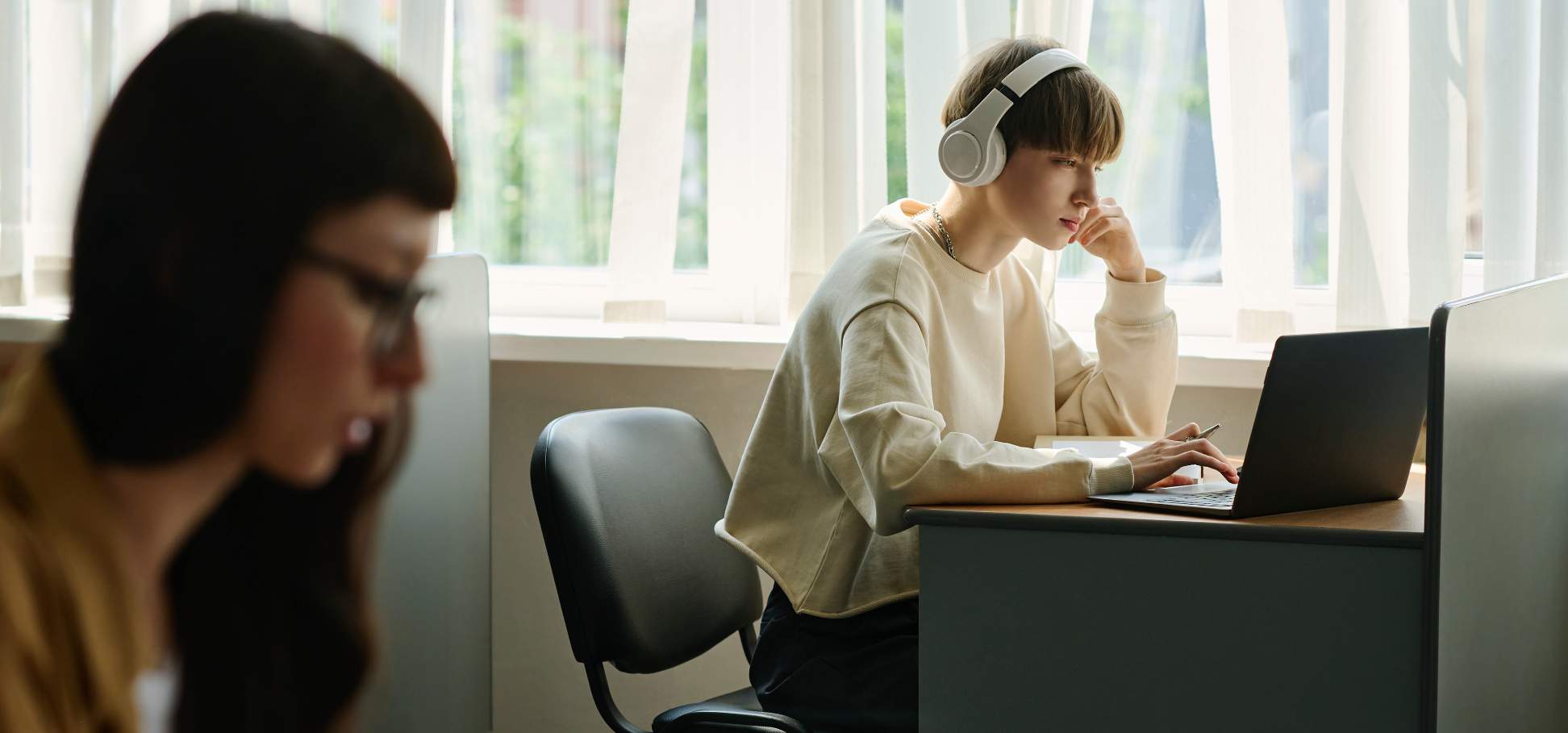 Zwei junge Frauen, eine davon mit Kopfhörer, konzentriert bei der Arbeit am Laptop.