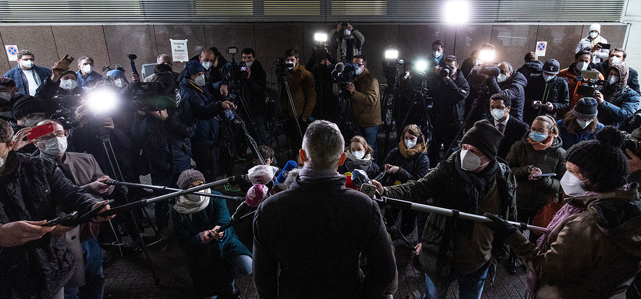 Foto einer Interviewsituation, bei der zahlreichen Journalistinnen und Journalisten sich einer männliche Person zuwenden, die nur von hinten sichtbar ist.